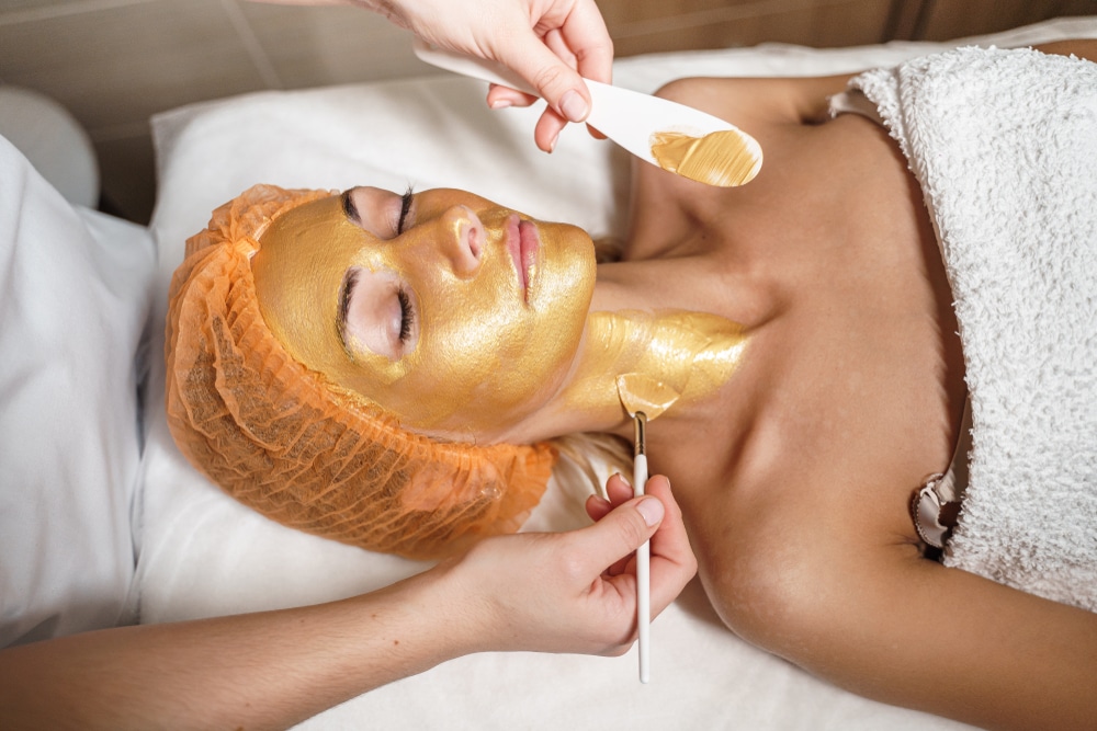 Image of a golden face mask being applied to a woman.